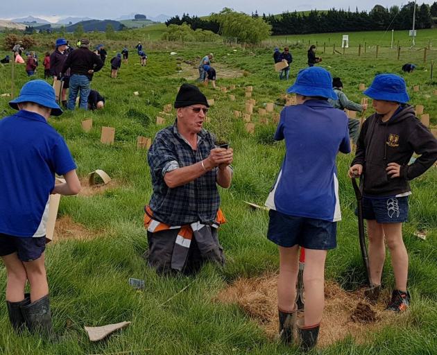 Gary Ross, of the Waiareka Valley Lions Club, helps children at a planting day in North Otago.