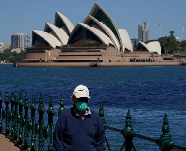 A person in a face mask walks along the harbour waterfront across from the Sydney Opera House....