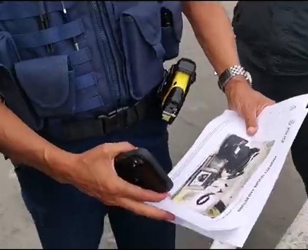 A police officer with an image of a toiletry bag shown to Tamaki supporters. Image via NZ Herald 