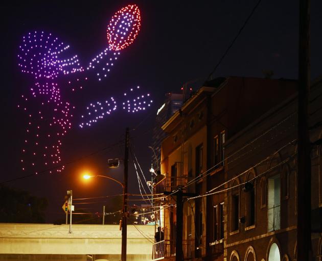 A person watches from a fire escape as drones fly in the shape of a footballer at the first Super...