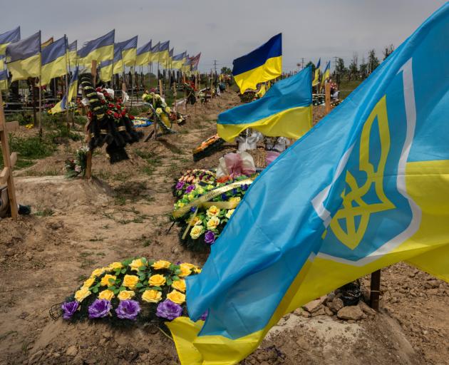 Flags of newly slain Ukrainian soldiers fly next to the graves of previously fallen troops in a...