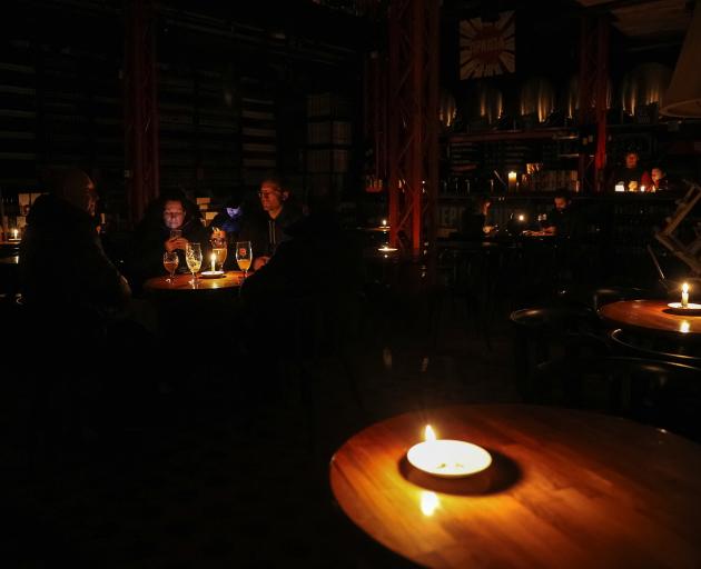 People sit in a pub lit with candles during a power outage after critical civil infrastructure...