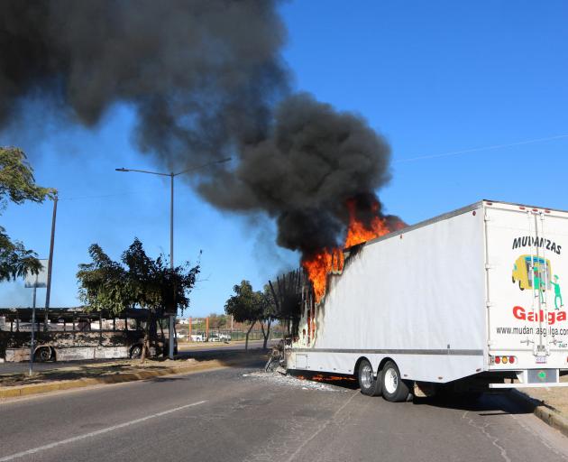 The burnt wreckage of a bus and a burning truck, set on fire by members of a drug gang are...