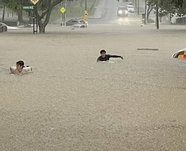 Young people on surfboards in the floodwaters in Grey Lynn. Photo / Supplied