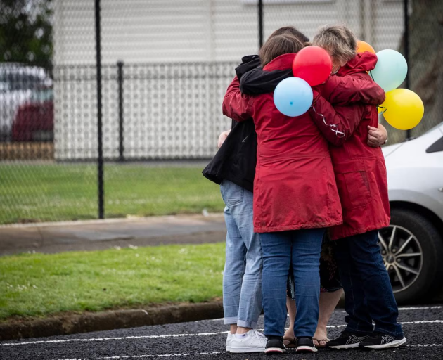 Mourners embrace outside Tuakau School this morning as a procession takes place following the...