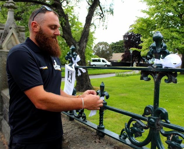 Chris Moore, of Isaac Construction, ties a white ribbon to the fence of First Church of Otago...