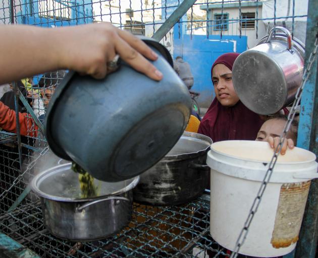 Palestinians wait to receive a free meal of Khobiza, a wild leafy vegetable, during the holy...