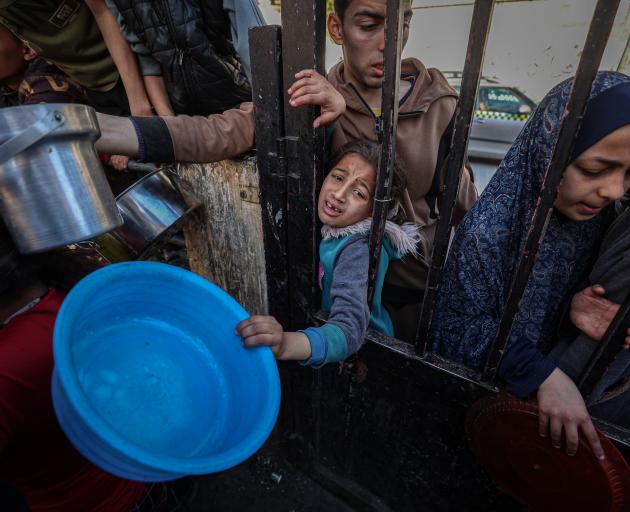 Displaced Palestinians wait to receive food cooked by a charity kitchen amid shortages of food...