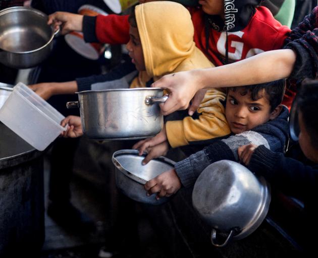 Palestinian children wait to receive food cooked by a charity kitchen amid shortages of food...