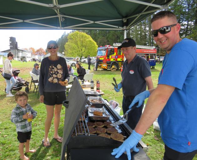 Attendees, pictured at left, enjoy a sausage in a blanket from barbecue masters Owen Wylie, left,...