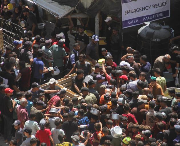 Palestinians gather to receive food cooked by a charity kitchen, near the ruins of houses...
