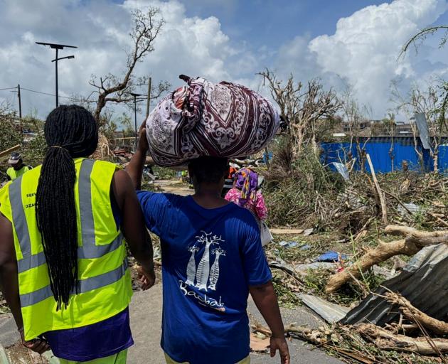 A man carries his belongings as rescue workers attempt to clear a blocked road in the aftermath...