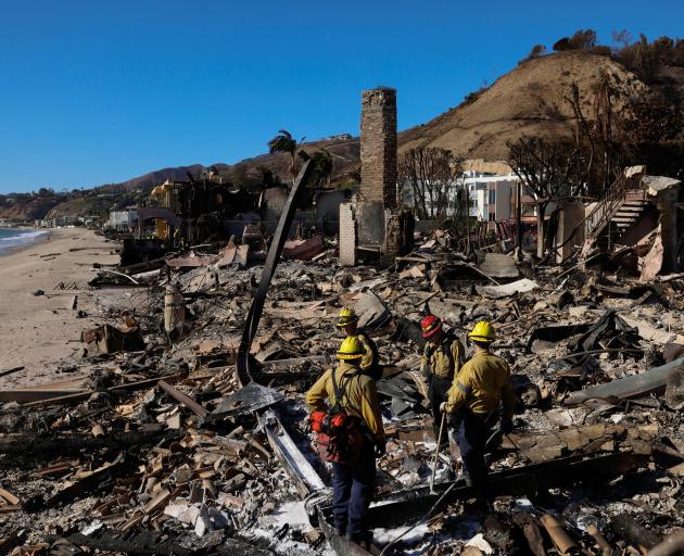 Firefighters dampen hotspots amid the remains of a home destroyed by the Palisades fire in Malibu...