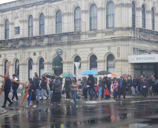 About 70 people walked behind a cross through the town’s central business district of Thames St....