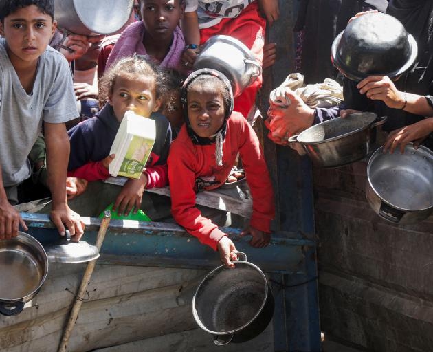 Palestinian children wait to receive food cooked by a charity kitchen in Khan Younis, Gaza. Photo...