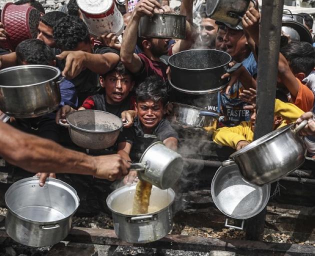 Hungry Palestinians wait to receive meals distributed by a charity organisation in Jabalia...
