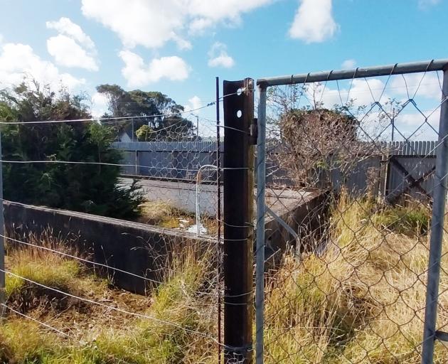 An empty swimming pool sits at the reserve along with changing rooms, the school building, and a...