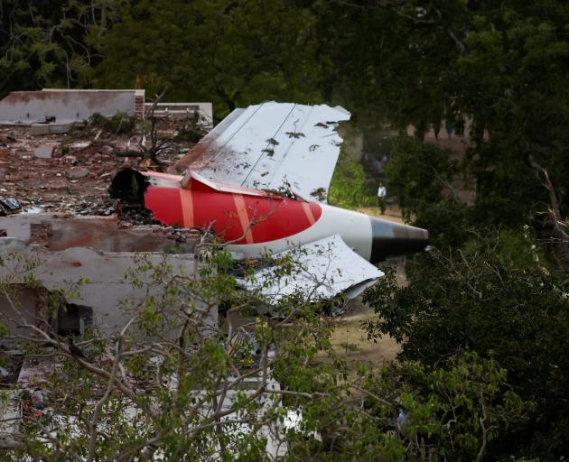 The tail of an Air India Boeing 787 Dreamliner plane that crashed is seen stuck on a building...