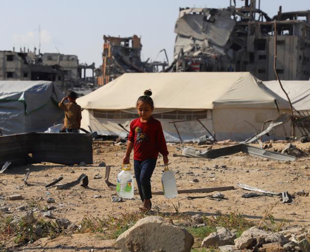 A displaced Palestinian girl carries water containers near tents in Gaza City as a fragile...