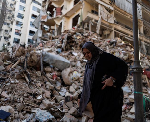 A woman walks past a damaged building at the site of an Israeli strike at Corniche al-Mazraa in...