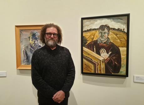 "Persona" curator Jim Geddes in the gallery of portraits. To his left is an Alan Pearson portrait...