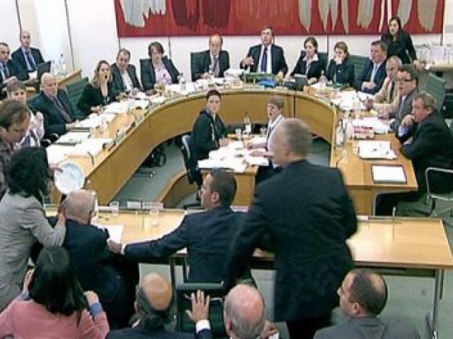 Committee members react after a protester, left in checked shirt, named on Twitter as Jonnie Marbles, tries to throw a paper plate covered in shaving foam over Rupert Murdoch.(AP Photo/pa) 