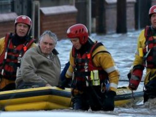 Emergency rescue service workers evacuate a resident in an inflatable boat in flood water in a residential street in Rhyl, north Wales. REUTERS/Phil Noble