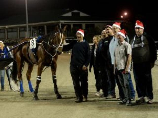Father Christmas and his connections gather in the winner’s circle at Forbury Park last night. Bev Williamson congratulates her son, driver Brad Williamson, at left as trainer Phil Williamson holds the reins. Photo by Linda Robertson.