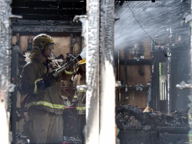 A firefighters dampens down hot spots in a charred house in Waikouaiti yesterday. Photo: Craig...