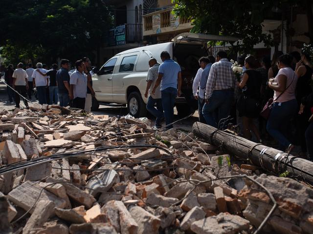 People walk by debris during a funeral ceremony held for a person that died in the earthquake in...