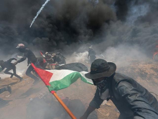 Palestinian demonstrators run for cover from Israeli fire and tear gas during a protest against...
