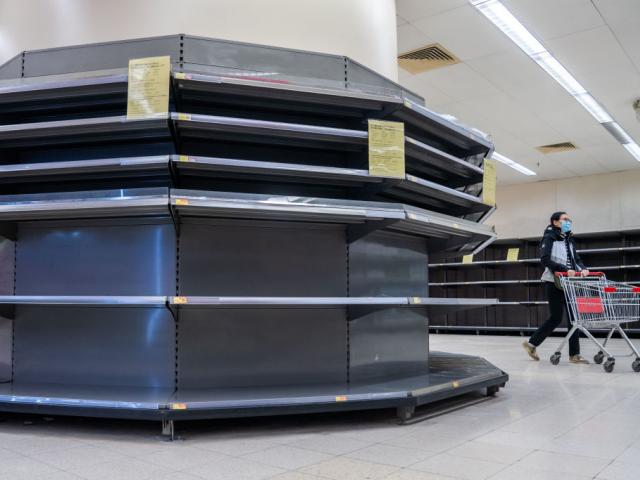 A female shopper in Hong Kong wearing a surgical mask walks past empty supermarket shelves,...