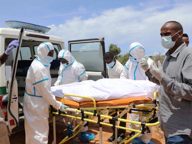 Somali workers in protective suits and civilians prepare to carry the body of a man suspected to...