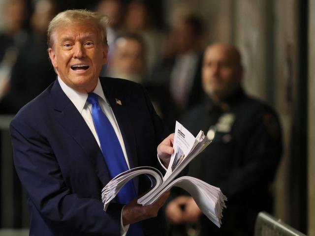 Donald Trump speaks to the media while holding a stack of news clippings at a New York court....