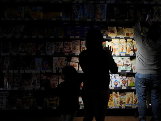 People use their phones and head torches to buy groceries inside the supermarket during the...