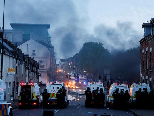Officers stand guard behind police vehicles during clashes on the second night of riots in...