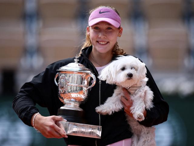 Russia's Mirra Andreeva celebrates with the trophy and a dog after winning her final match...