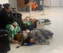 A mother looks on as her young daughter sleeps on the cold floor after arriving on a flight from...