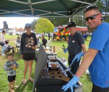 Attendees, pictured at left, enjoy a sausage in a blanket from barbecue masters Owen Wylie, left,...