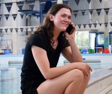 Erika Fairweather takes a call pool-side under neath a sign for Dunedin Olympic champion Danyon...