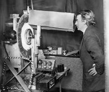 John Logie Baird peers into a receiving machine to view an image of a living and moving face, in...