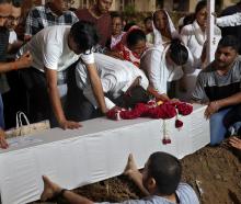 Relatives of one of the crash victims lower a coffin containing his remains into a grave at a...