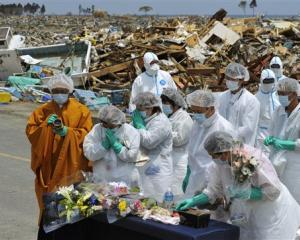 A Buddhist monk and residents pray in front of a makeshift incense stand in Namie, northeastern...