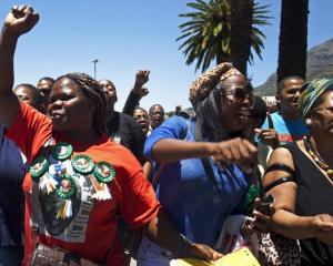 A woman with a Nelson Mandela t-shirt and badges sings and dances along with others in front of...