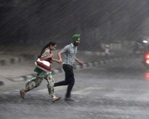 Commuters run for cover as they cross a road during monsoon rains in the northern Indian city of...