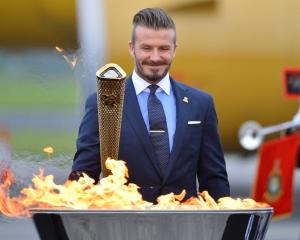 David Beckham, a London 2012 Olympic Games ambassador, reacts after lighting the Olympic torch...