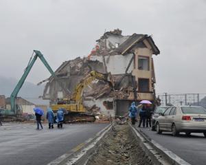 Excavators demolish the house of Luo Baogen in the middle of a newly built road in Wenling,...