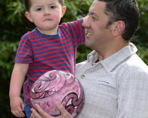 Manuaitu Haggie (2) at home with his father, Reihana, and the carved bowling ball up for auction....