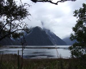 Mitre Peak hides its face behind a veil of cloud as a tourist vessel returns from an excursion on...