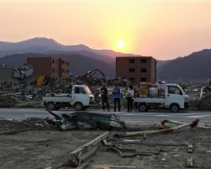 People stand among the rubble in the area devastated by the Match 11 earthquake and tsunami in...